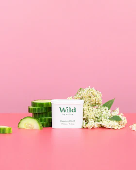 Caption: a pink table with a container of wild and a cucumber next to it
