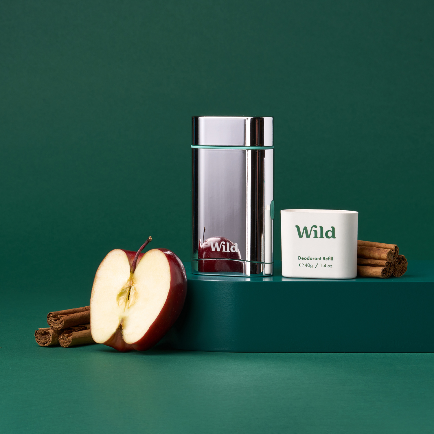 Pie de foto: una manzana, canela en rama y un vaso de agua sobre una superficie verde.