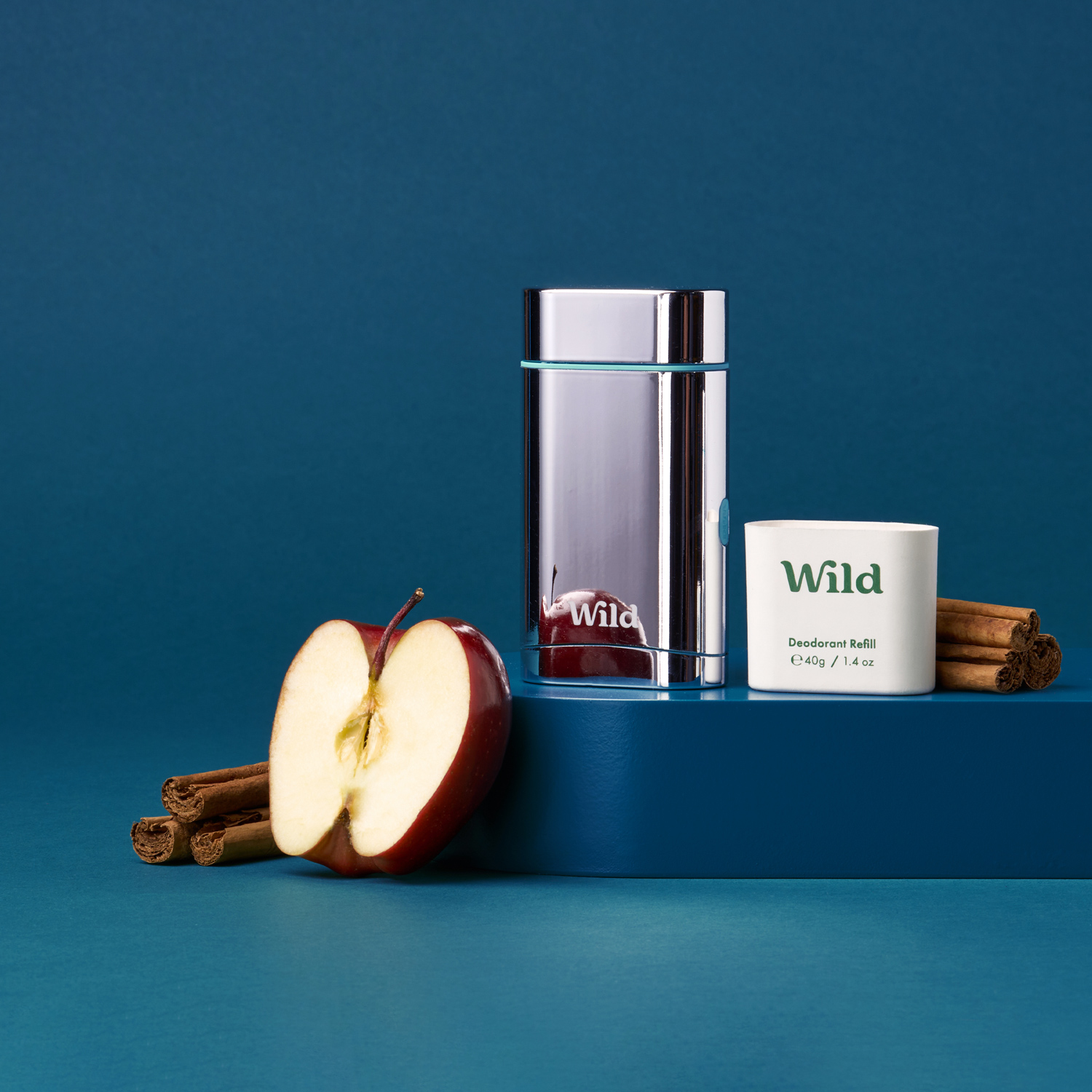 Pie de foto: una manzana, canela en rama y un vaso de agua sobre una superficie azul.