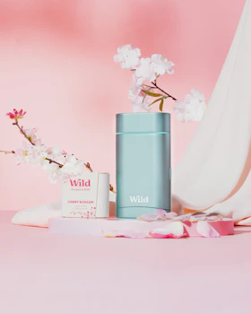 Caption: a pink background with a vase of flowers and a bottle of wild