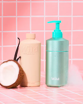 Caption: a bottle of lotion next to a coconut on a pink tiled surface