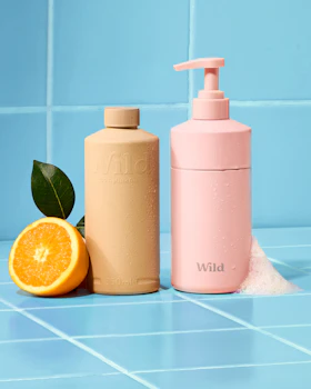 Caption: a bottle of lotion next to an orange on a blue tiled counter