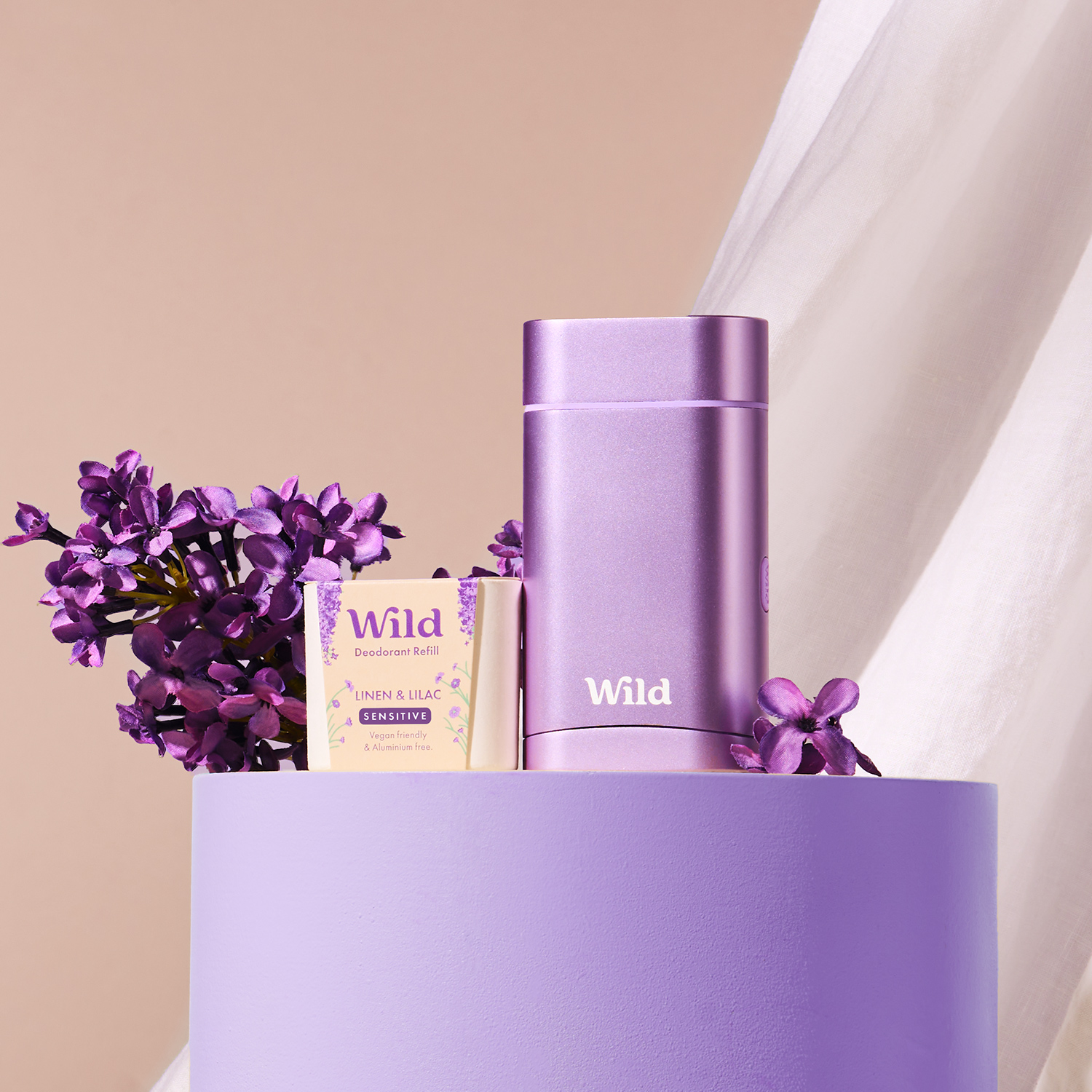 Bildunterschrift: eine violette Vase, gefüllt mit violetten Blumen, neben einem weißen Vorhang