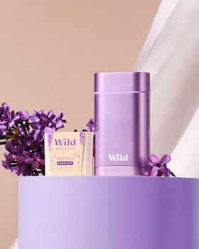 Caption: a purple vase filled with purple flowers next to a white curtain