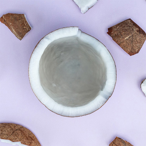 Légende : un bol blanc rempli de noix de coco sur une surface violette.