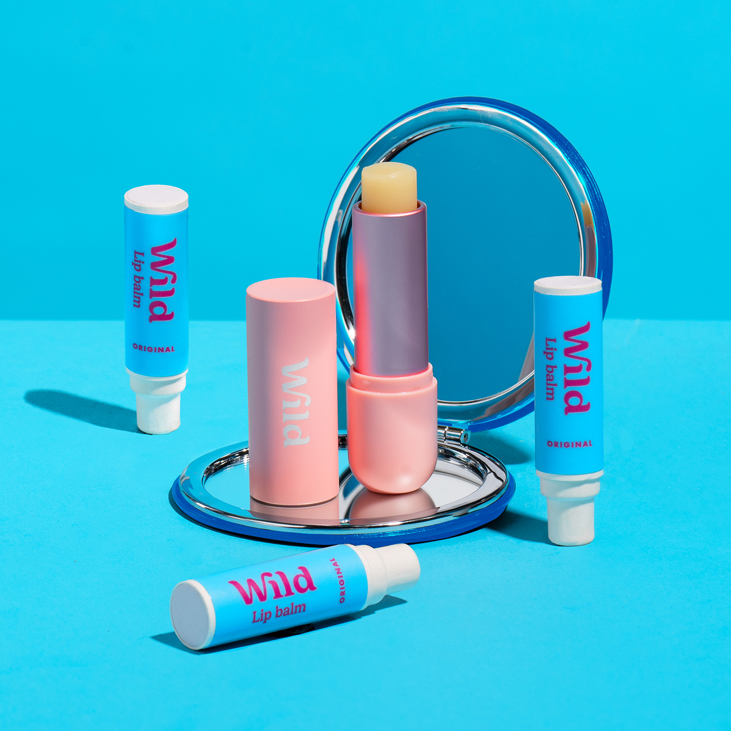 Bildunterschrift: ein Spiegel und einige Lippenballen auf einer blauen Fläche