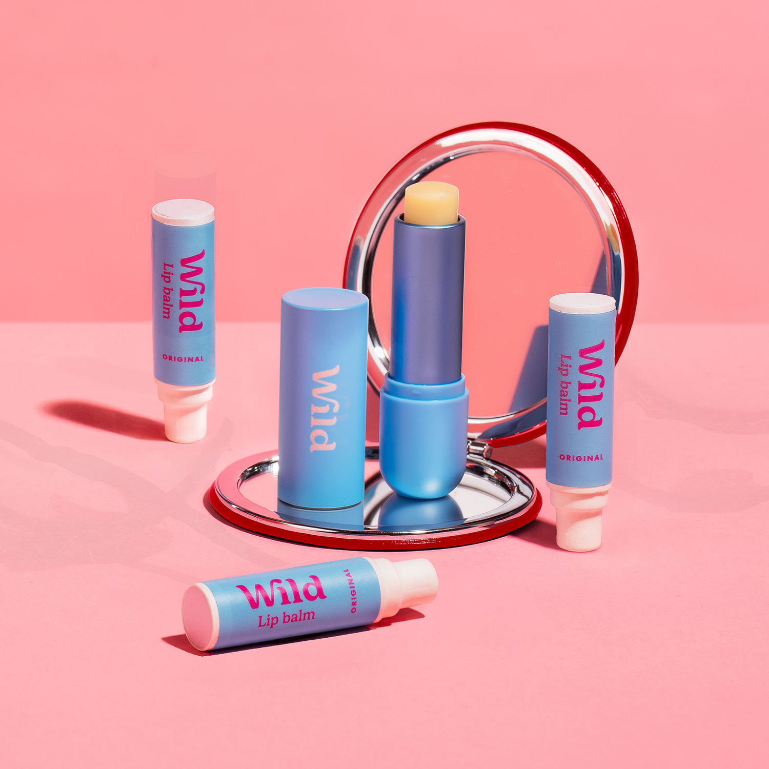 Bildunterschrift: rosa Hintergrund mit einem Spiegel und drei Lippenballen