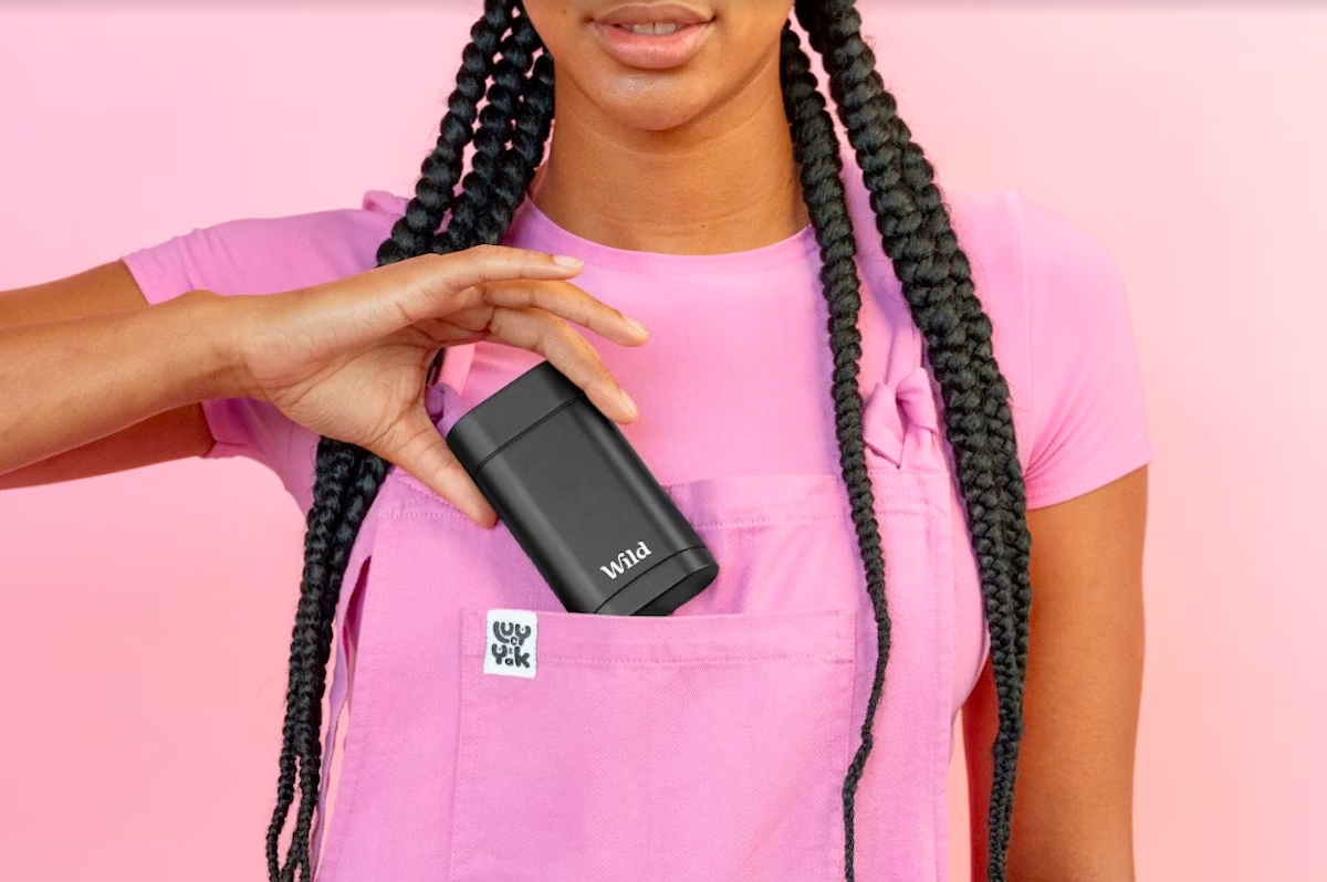 Bildunterschrift: eine Frau in einem rosa Hemd, die ein Handy hält