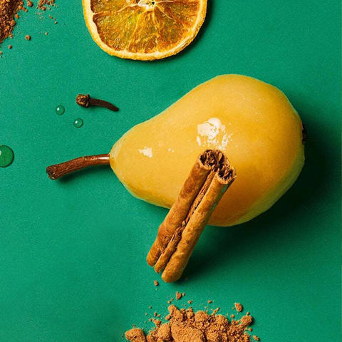 Caption: a pear, cinnamon, and orange on a green surface