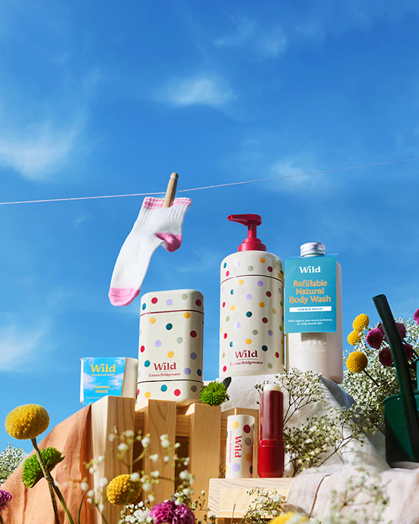 Wild Cosmetics products arranged on wooden blocks and surrounded by flowers, on a sunny day with a blue sky.