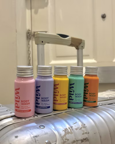 Five bottles of Wild Cosmetics body wash in different pastel colors (pink, purple, yellow, teal, orange) lined up on a stainless steel surface.