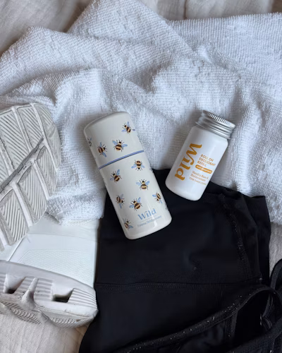 Wild Bee roll-on deodorant case and refill on top of black leggings and sneakers, lying on a white textured surface