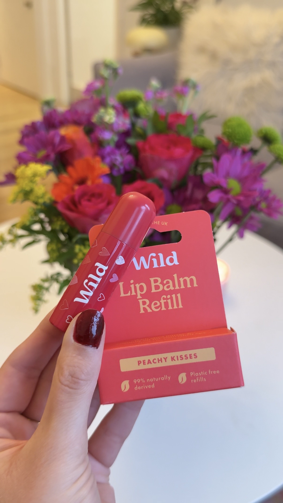 Caption: a person holding a lip balm in front of a bouquet of flowers