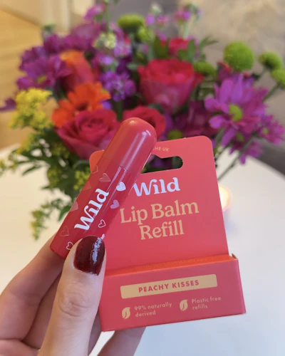 Caption: a person holding a lip balm in front of a bouquet of flowers