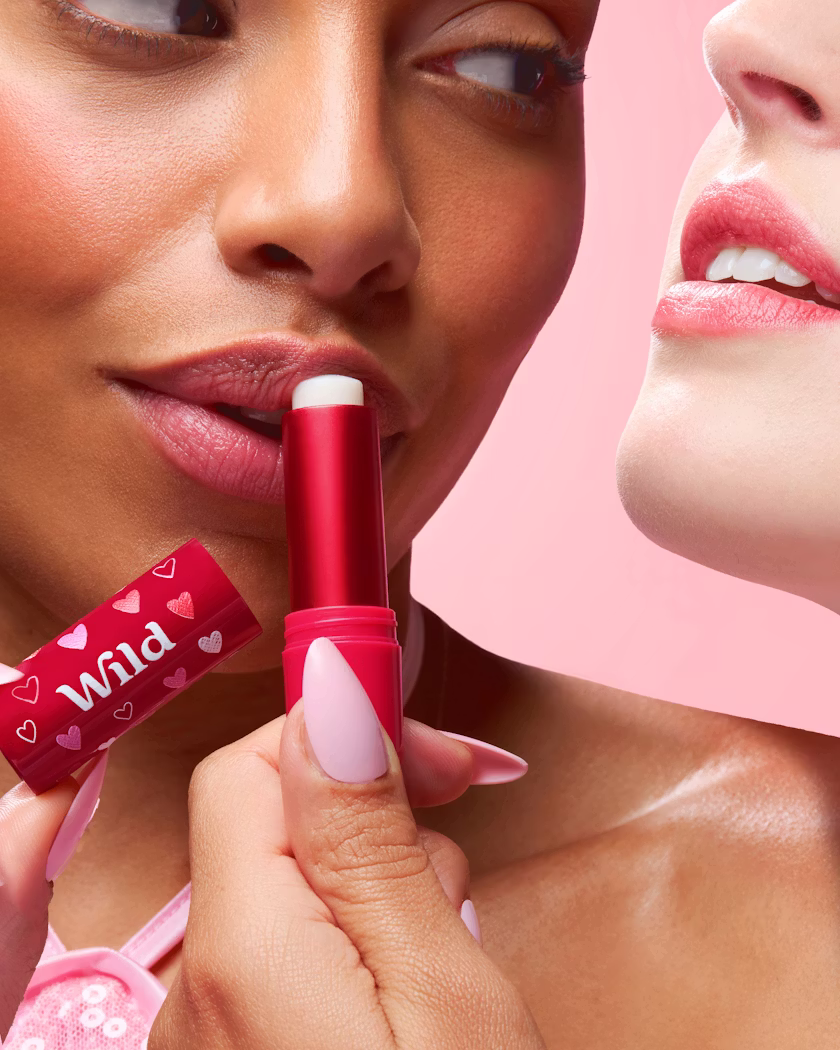 Caption: a woman putting lipstick on another woman's lips