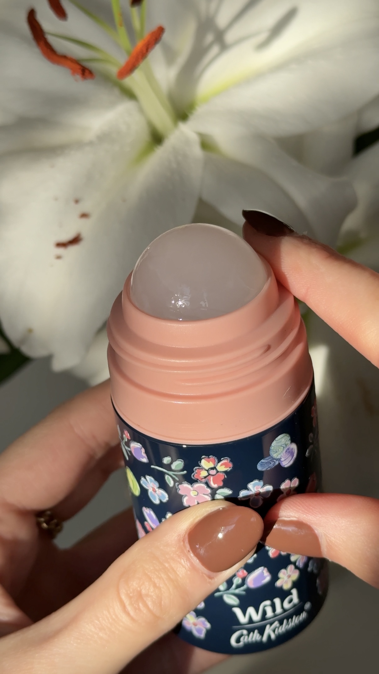 Caption: a woman holding a bottle of lip bale next to a flower