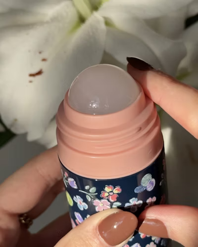 Caption: a woman holding a bottle of lip bale next to a flower