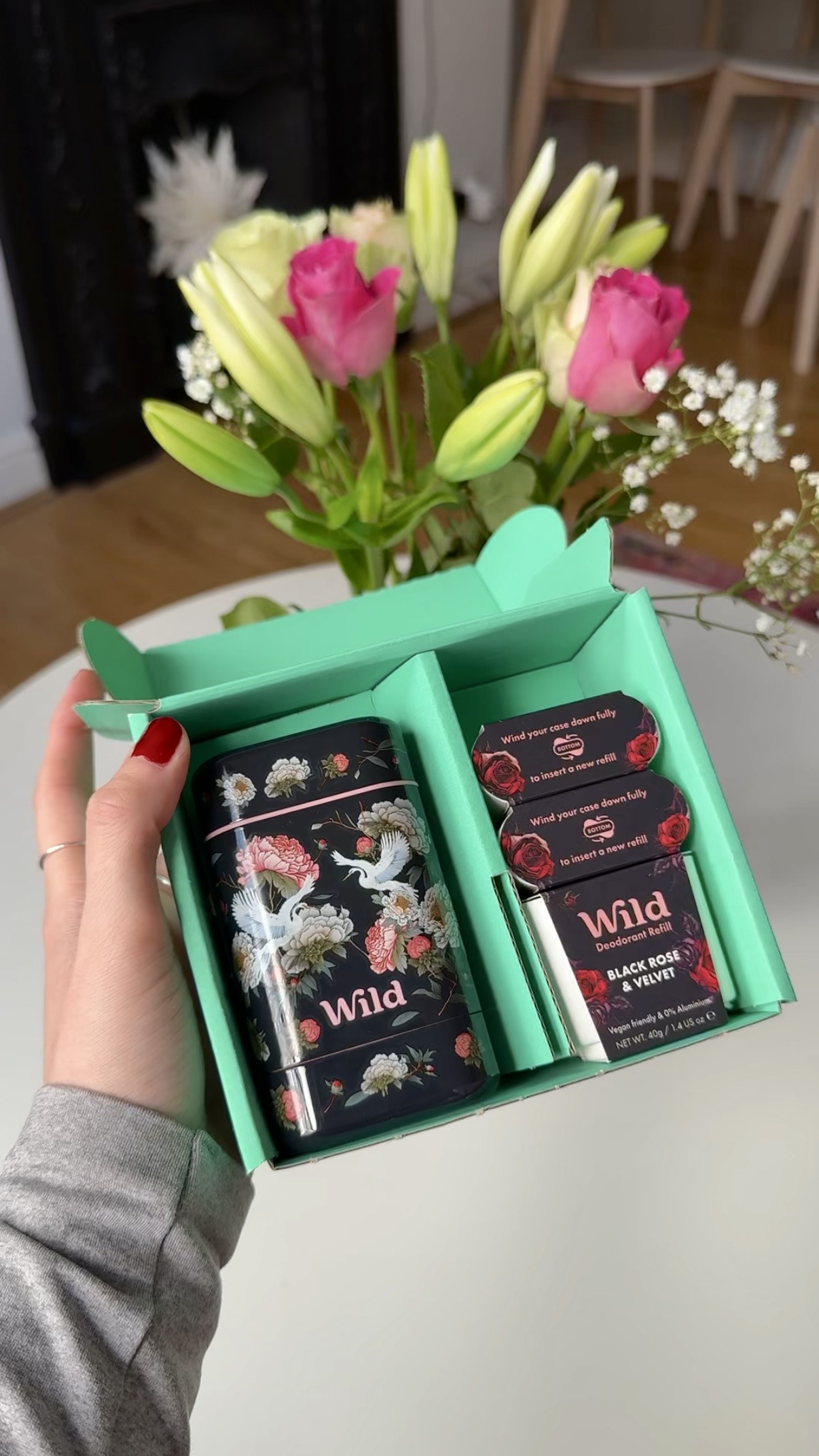 Caption: a person holding a box of chocolates in front of a vase of flowers