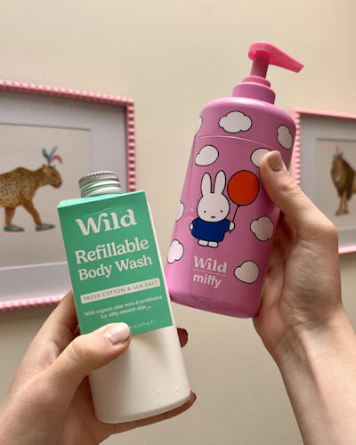 Bildunterschrift: Eine Person, die eine rosa-weiße Flasche und einen rosa-weißen Becher in der Hand hält
