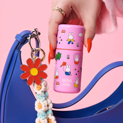 Bildunterschrift: Die Hand einer Frau, die eine rosa-blaue Handtasche und eine rosa-weiße