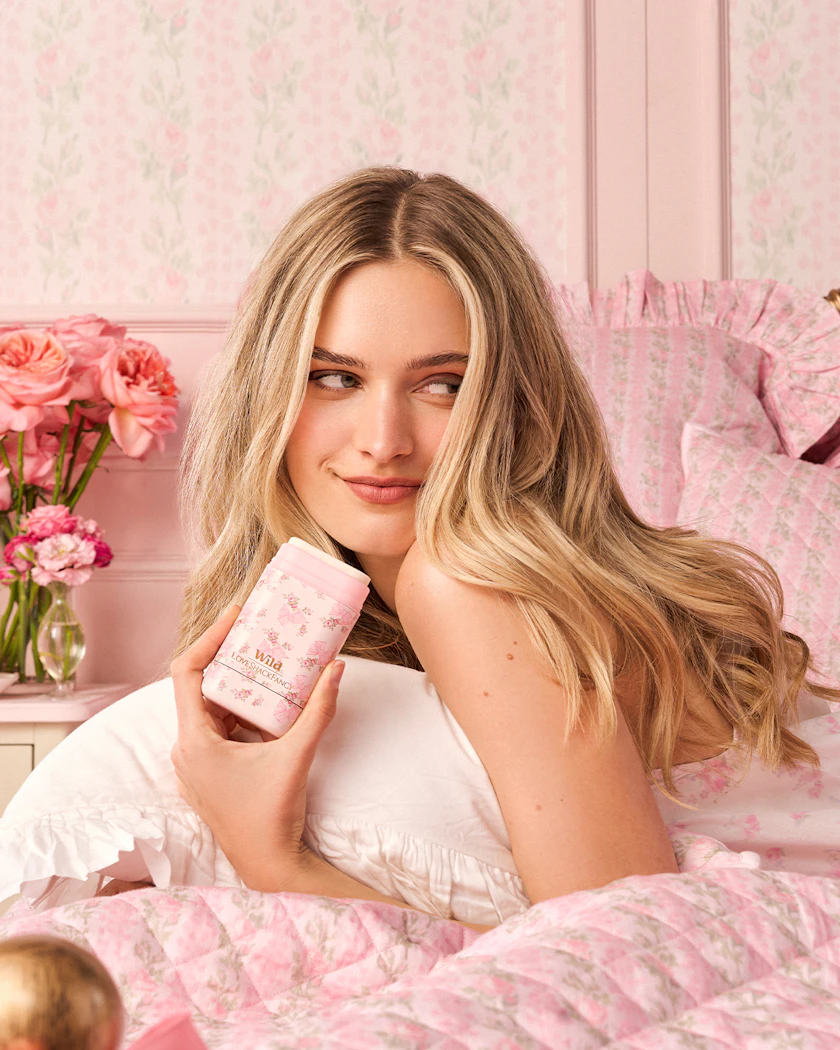 Caption: a woman laying on a bed holding a bottle of lotion