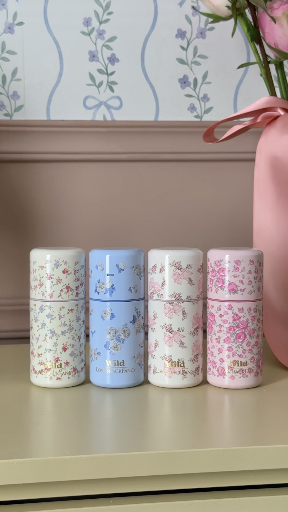 Caption: a pink vase with a pink flower in it and five different colored flowered boxes